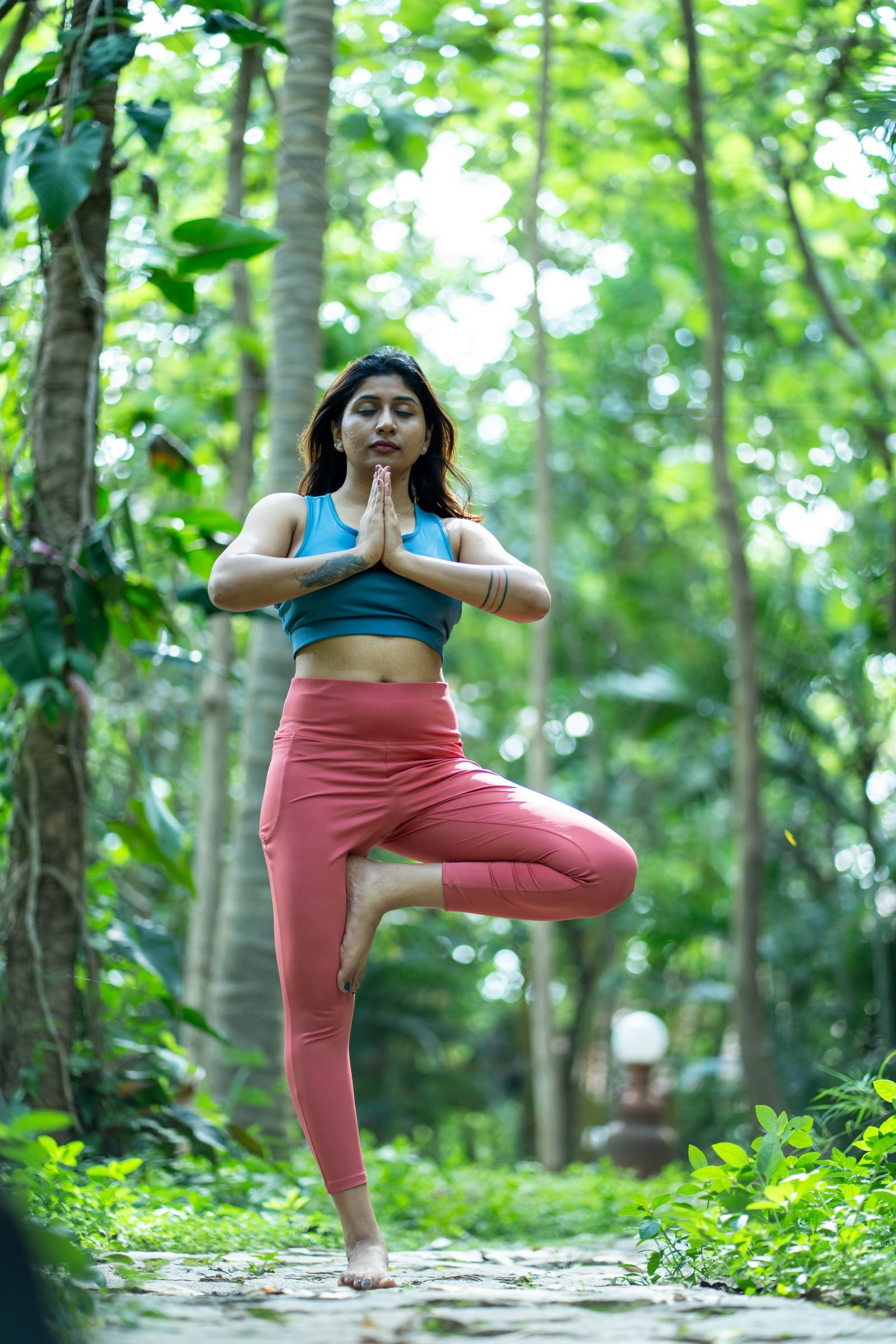 A woman practicing yoga outdoors in a green, forested space